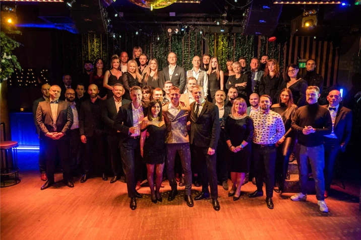 Duża grupa osób w eleganckich strojach pozująca na firmowym wydarzeniu w stylowym wnętrzu