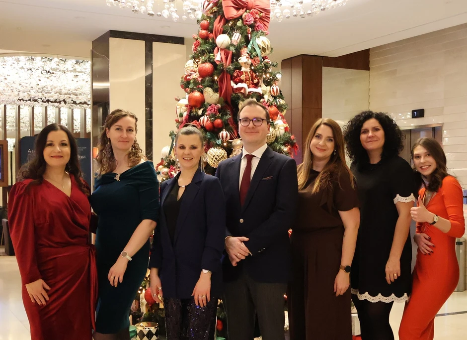 Zespół pracowników pozujący przy udekorowanej choince podczas firmowego przyjęcia świątecznego