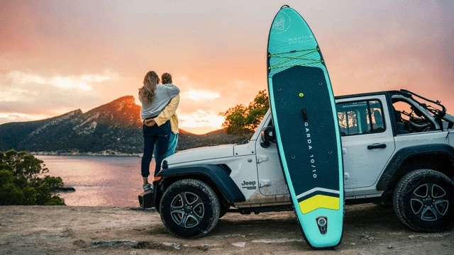Para podziwia zachód słońca przy białym jeepie z deską do paddleboardingu nad jeziorem i górami