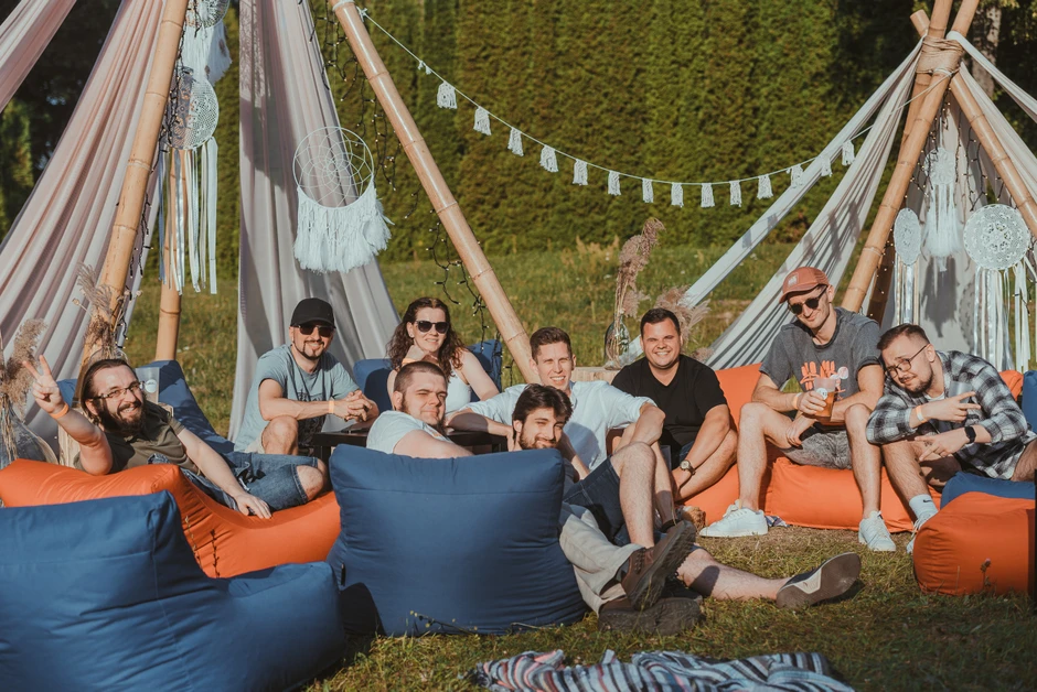 Grupa młodych ludzi relaksuje się na pufach w ogrodzie przy dekorowanych namiotach podczas firmowego wydarzenia