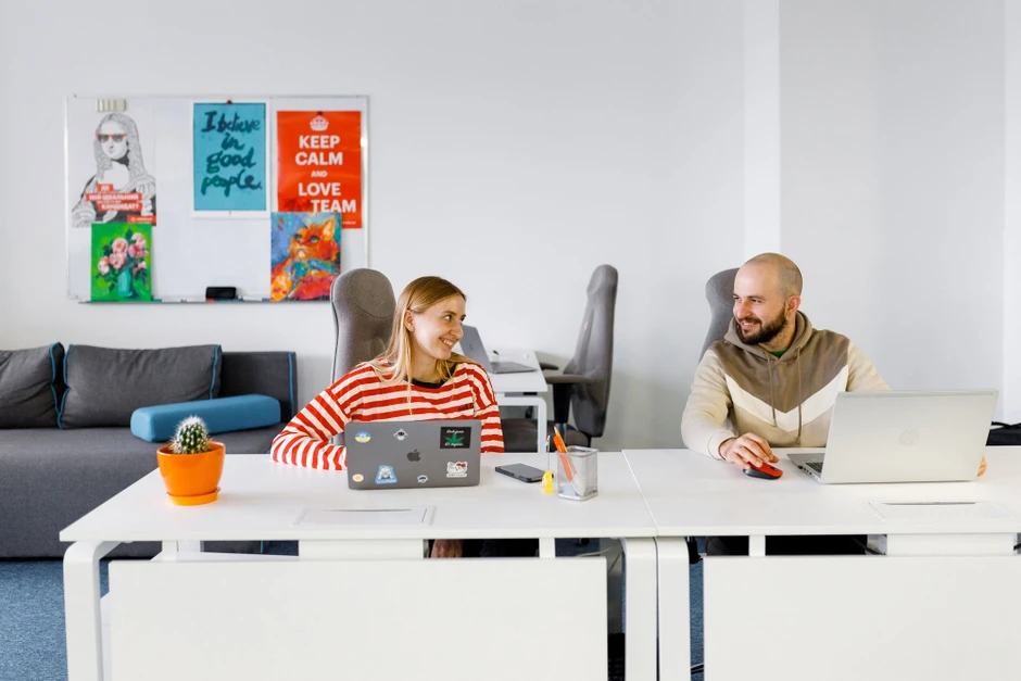 Dwoje pracowników rozmawia i uśmiecha się przy biurkach w jasnym nowoczesnym biurze