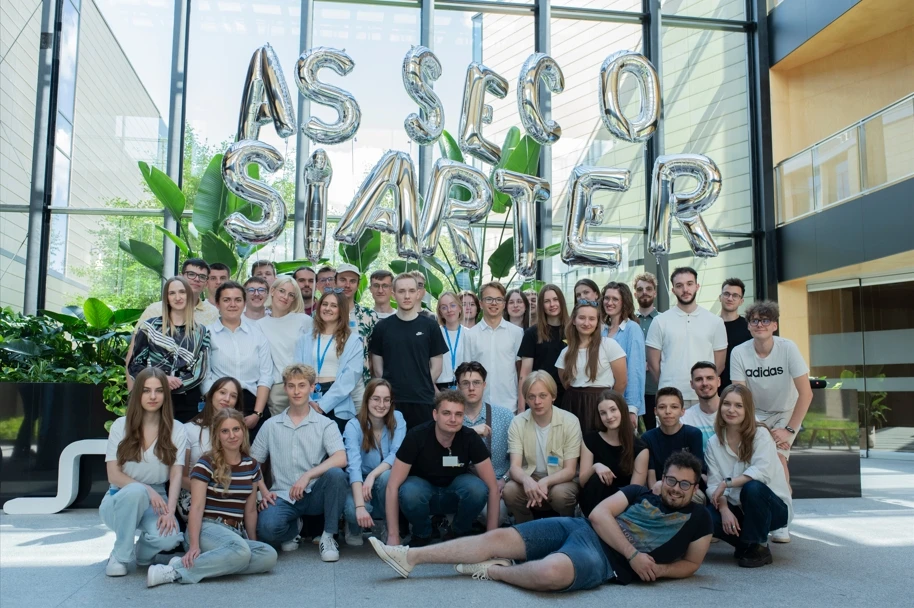 Grupa młodych ludzi pozująca w nowoczesnym biurze z balonami tworzącymi napis Asseco Starter