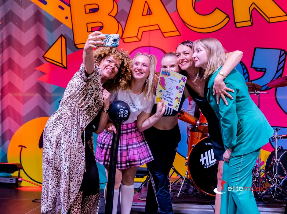 Grupa uśmiechniętych kobiet robiących selfie na imprezie z kolorowym tłem i muzyką na żywo