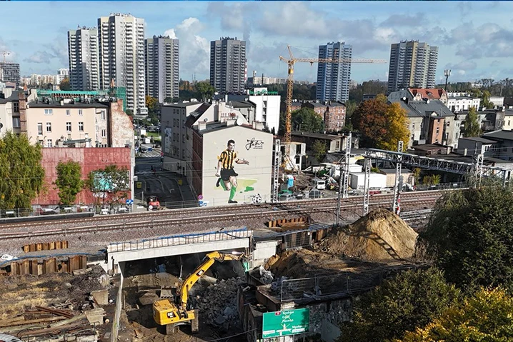 Budowa z rozkopanym placem i maszynami w miejskiej dzielnicy z wysokimi blokami i muralem piłkarza na ścianie