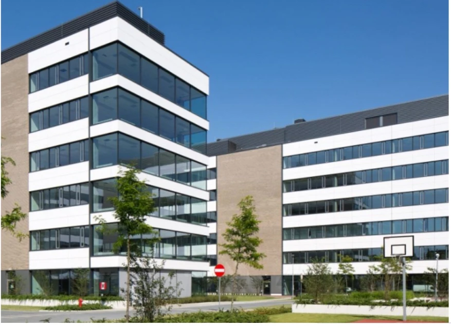 Nowoczesny budynek biurowy z dużymi oknami i zielenią na terenie firmy