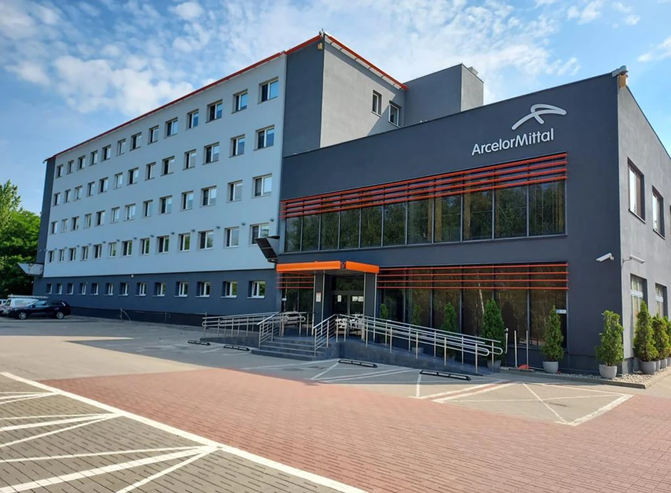 Nowoczesny budynek biurowy ArcelorMittal z dużymi oknami i przestronnym parkingiem na tle nieba