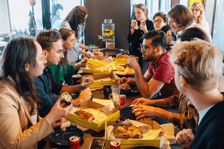 Grupa pracowników wspólnie je pizzę podczas nieformalnego spotkania integracyjnego w biurze
