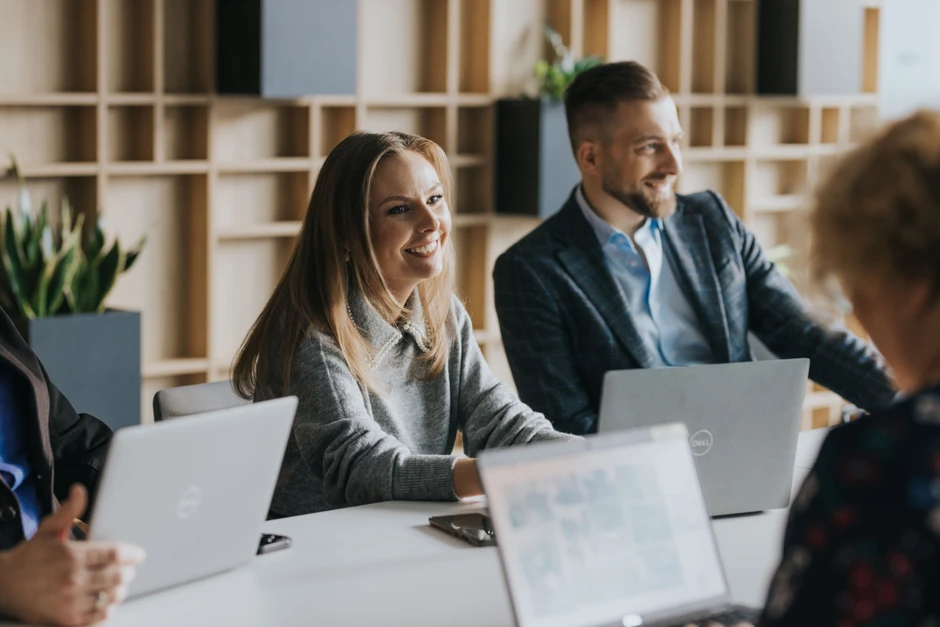 Zespół pracowników podczas spotkania biznesowego w nowoczesnym biurze z laptopami i uśmiechami