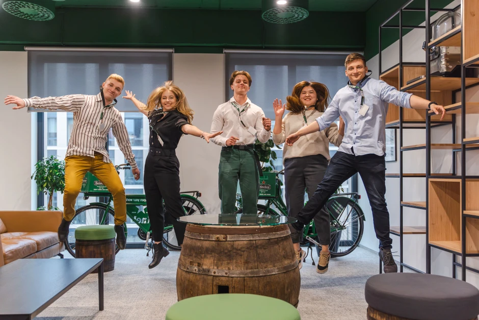 Grupa młodych ludzi skaczących radośnie w nowoczesnym biurze z rowerami i drewnianymi meblami