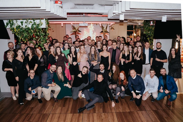 Duża grupa osób w eleganckich strojach pozująca razem podczas firmowego wydarzenia w nowoczesnym wnętrzu