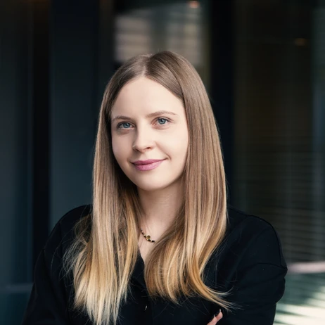 Portret młodej kobiety o długich blond włosach ubraną w czarny sweter na tle biurowego wnętrza