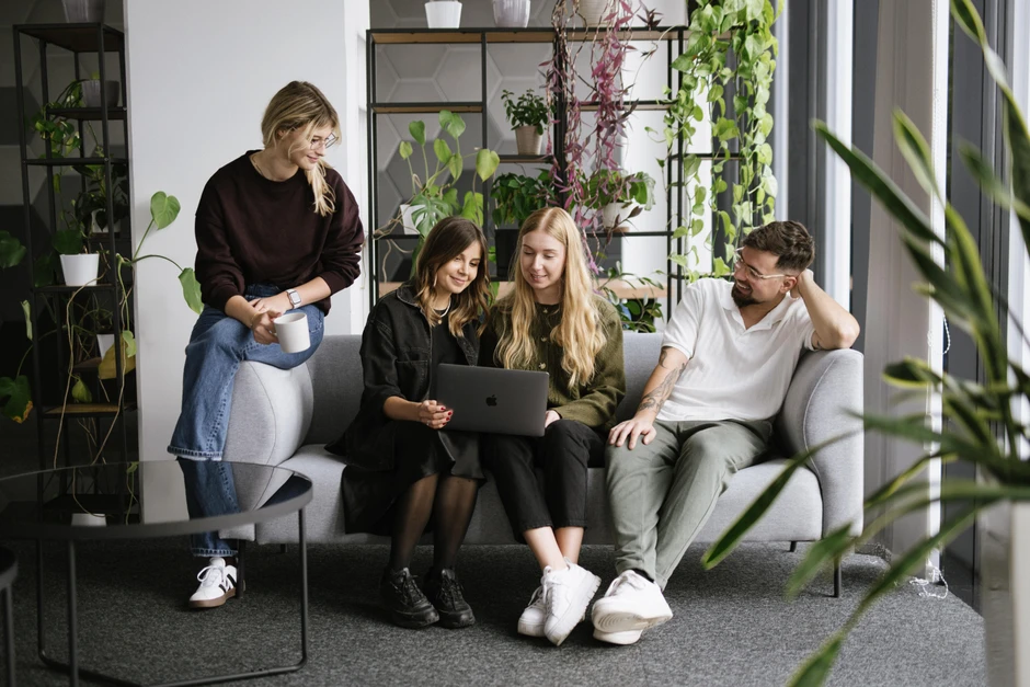 Cztery osoby w nowoczesnym biurze razem oglądają coś na laptopie na kanapie między roślinami