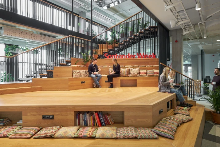 Przestronne biuro z drewnianymi schodami, kolorowymi poduszkami i pracownikami podczas rozmowy