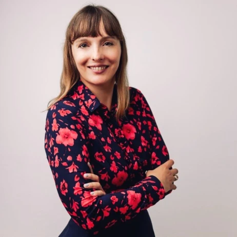 Uśmiechnięta kobieta w granatowej koszuli w czerwone kwiaty na jasnym tle, ze skrzyżowanymi rękami