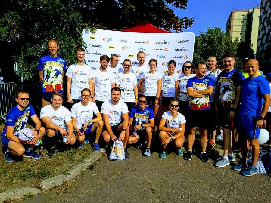 Zespół biegaczy w firmowych koszulkach pozujący razem przed ścianką eventową na świeżym powietrzu