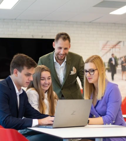 Czterech współpracowników omawia projekt przy laptopie w nowoczesnym biurze z uśmiechem