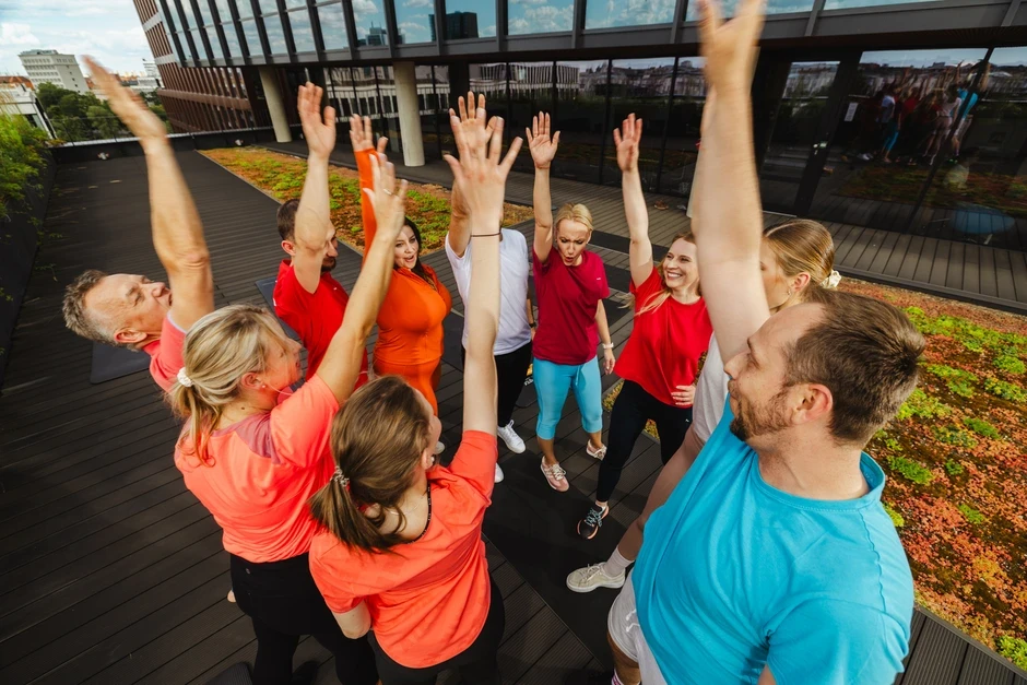 Zespół pracowników na zewnątrz podnosi ręce w geście integracji i pozytywnej energii przed budynkiem biurowym