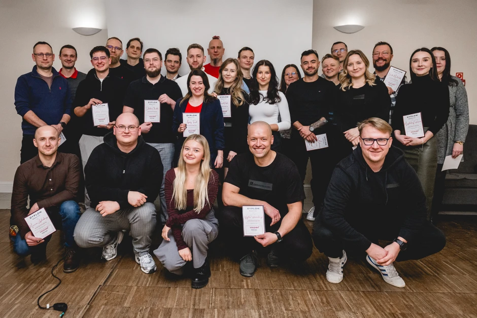 Grupa pracowników firmy pozująca do zdjęcia z dyplomami w jasnym pomieszczeniu podczas uroczystości