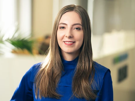 Uśmiechnięta kobieta w niebieskiej bluzce na tle jasnego, nowoczesnego biura