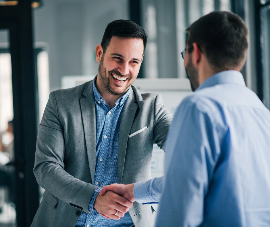 Dwóch mężczyzn uśmiechających się podczas uścisku dłoni w nowoczesnym biurze firmowym