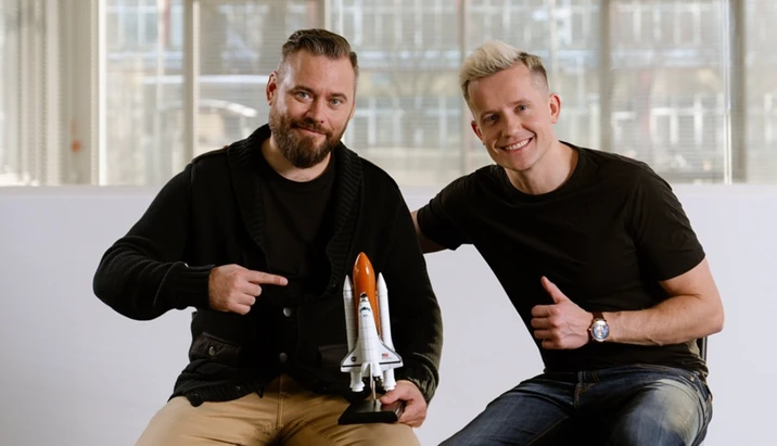 Dwóch uśmiechniętych mężczyzn prezentuje model promu kosmicznego w nowoczesnym biurze