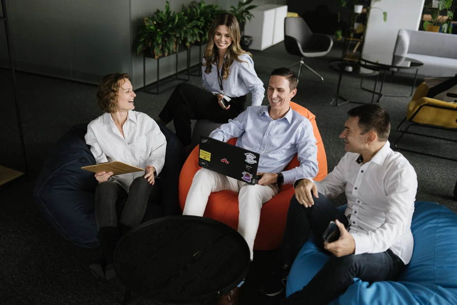 Grupa pracowników w luźnej atmosferze omawia projekt siedząc na pufach w nowoczesnym biurze