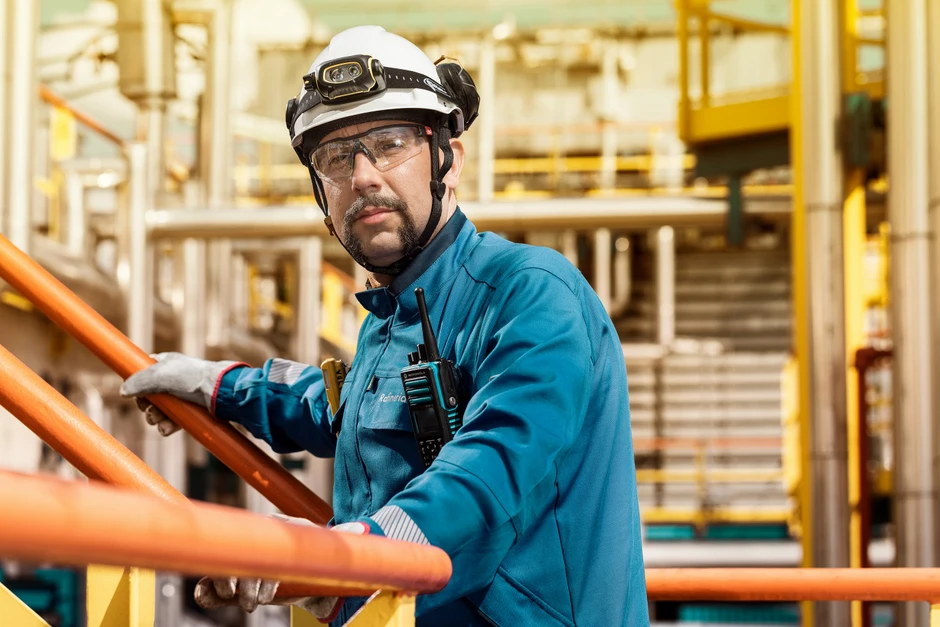 Pracownik przemysłowy w kasku i okularach ochronnych na terenie zakładu produkcyjnego trzyma się barierki