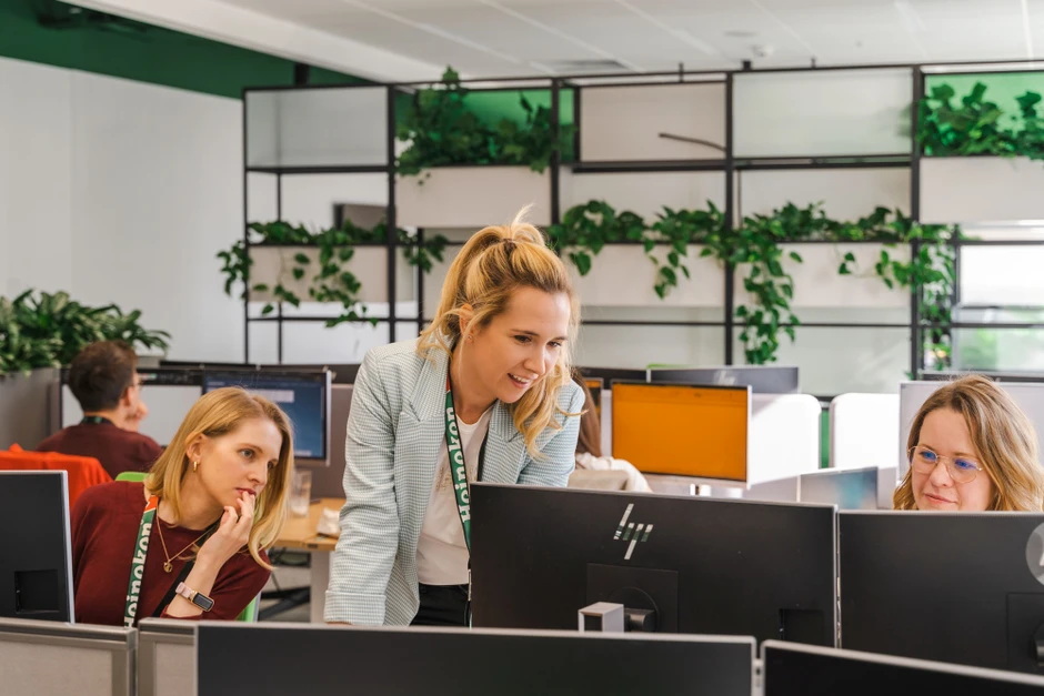 Trzy kobiety współpracują przy komputerach w nowoczesnym biurze z zielonymi roślinami na tle