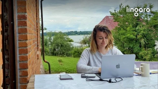 Kobieta pracuje przy laptopie na zewnątrz w otoczeniu zieleni i widokiem na jezioro w tle