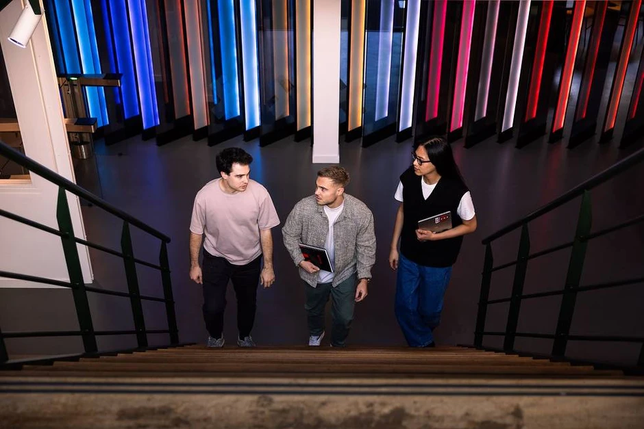 Trzech młodych pracowników rozmawia i spaceruje razem po nowoczesnym biurze z kolorowym oświetleniem