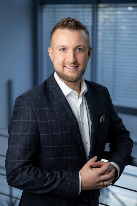 Portret uśmiechniętego mężczyzny w stylowym garniturze na tle biura z żaluzjami