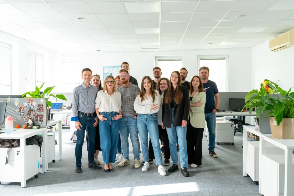 Zespół współpracowników pozujący w jasnym, nowoczesnym biurze pełnym zielonych roślin i naturalnego światła