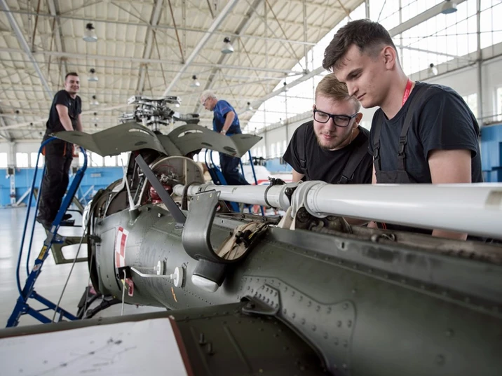 Pracownicy serwisują wojskowy śmigłowiec w jasnym hangarze podczas zespołowego szkolenia i naprawy