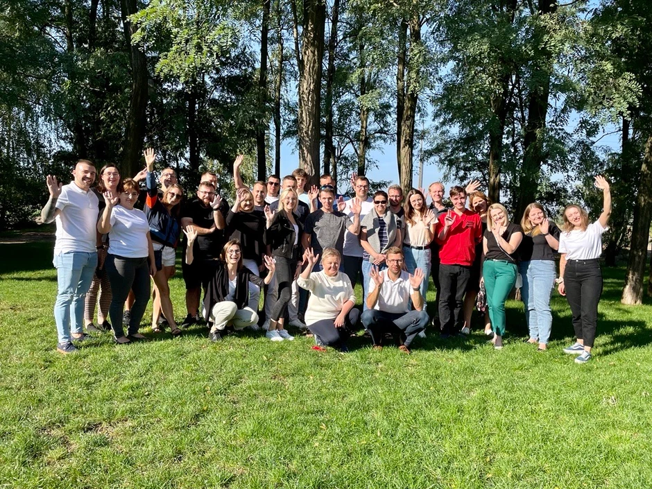 Zespół pracowników pozuje do zdjęcia na zielonej łące na tle drzew podczas słonecznego dnia