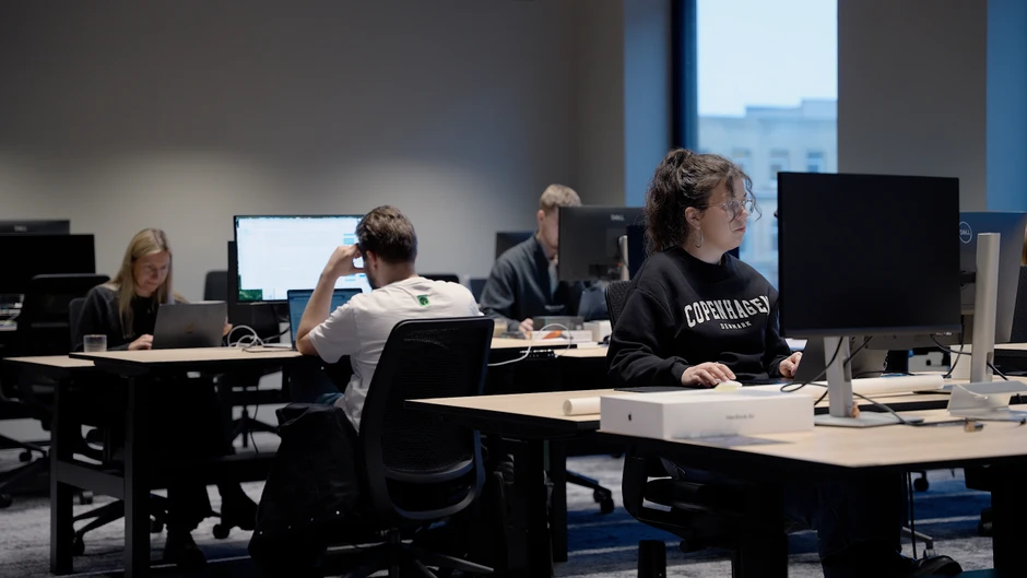 Pracownicy skupieni na pracy przed monitorami w nowoczesnym, cichym biurze z dużymi oknami