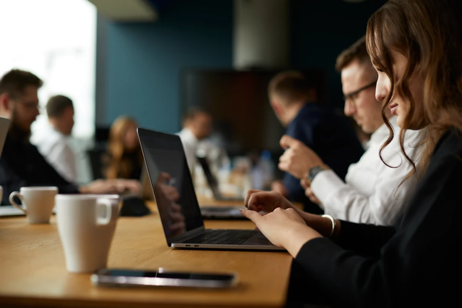Grupa pracowników podczas spotkania firmowego pracuje na laptopach przy dużym stole konferencyjnym