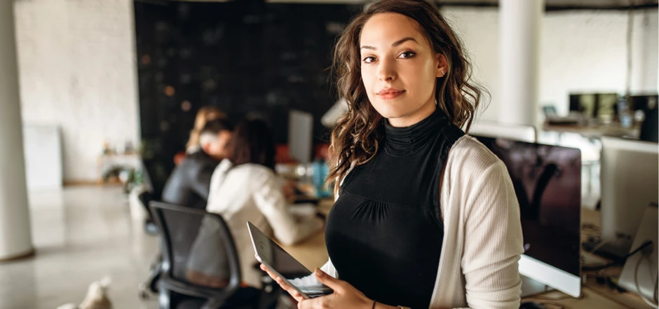 Młoda kobieta z tabletem w nowoczesnym biurze z zespołem pracującym w tle