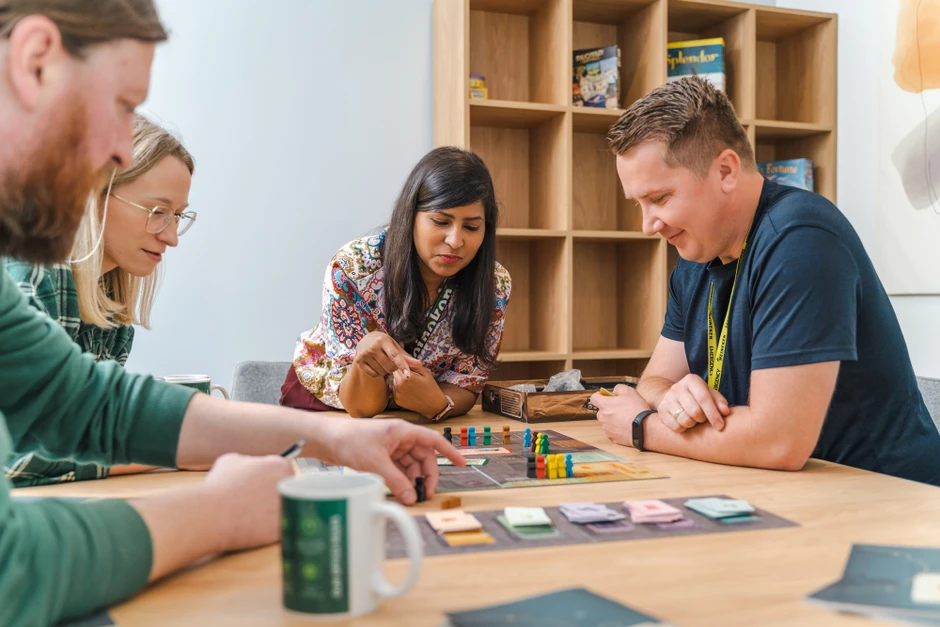 Cztery osoby z zaangażowaniem grają w grę planszową w przyjaznym biurowym otoczeniu