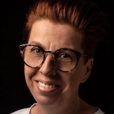 Portret uśmiechniętej osoby w okularach na czarnym tle, emanacja profesjonalizmu i przyjaznej atmosfery