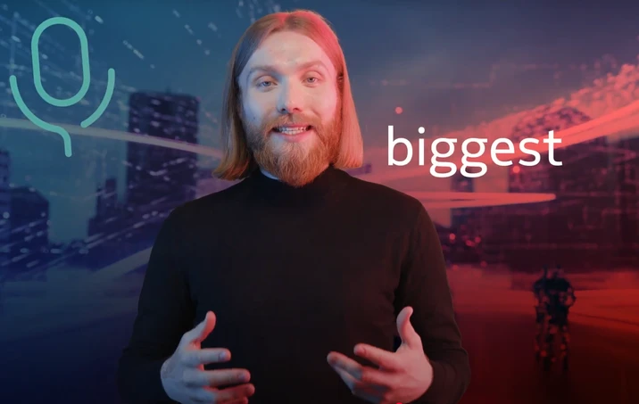 Mężczyzna z brodą i długimi włosami prezentuje coś na tle futurystycznego miasta z napisem biggest