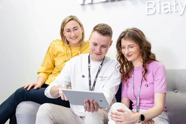 Trójka młodych pracowników omawia projekt na tablecie podczas spotkania w nowoczesnym biurze