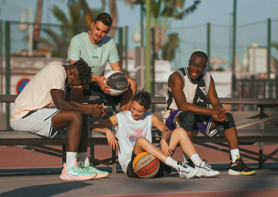 Grupa młodych ludzi odpoczywająca na boisku do koszykówki po wspólnej rozgrywce na świeżym powietrzu