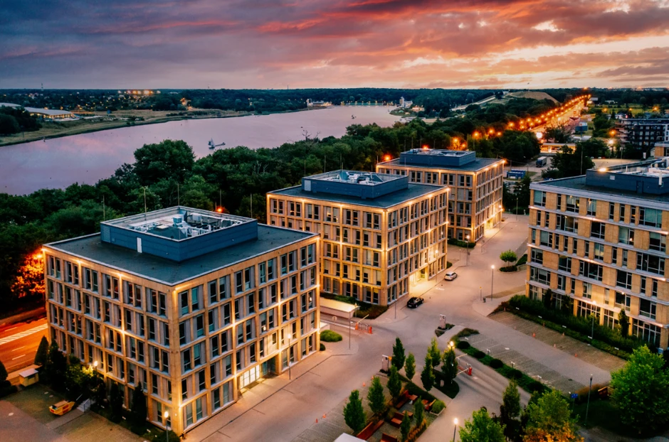 Nowoczesny kompleks biurowy nad rzeką oświetlony ciepłym światłem podczas zachodu słońca