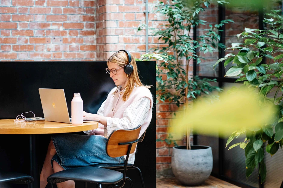 Młoda kobieta pracuje na laptopie w nowoczesnym biurze z ceglanymi ścianami i roślinami