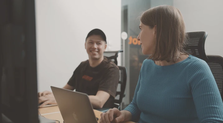 Dwóch pracowników rozmawia i uśmiecha się przy biurku z laptopem w nowoczesnym biurze