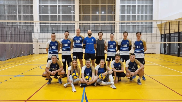 Zespół siatkarski pracowników w kompletnych strojach pozujący na hali sportowej z siatką w tle
