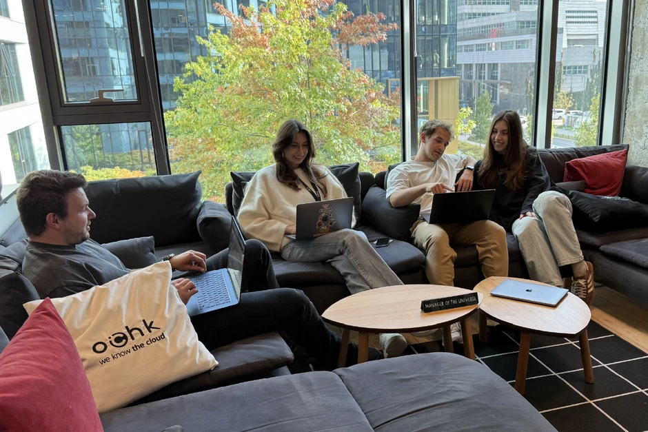 Zespół pracowników w nowoczesnym biurze dyskutuje i pracuje wspólnie na laptopach przy wygodnej kanapie