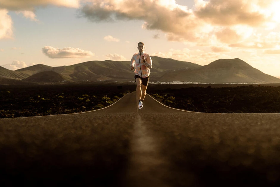 Mężczyzna biegnący pustą drogą o zachodzie słońca na tle gór i chmur z dala od miasta