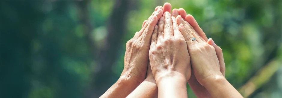 Wiele rąk złożonych razem symbolizujących współpracę i jedność zespołu na tle zieleni