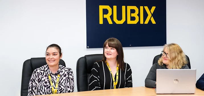 Trzy kobiety podczas spotkania w biurze firmy Rubix z widocznym logo na ścianie